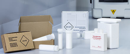 Links Post-Transportverpackung, daneben mehrere Schutzgefäße, rechts Kühlversandbehälter, im Hintergrund eine weitere Post-Transportverpackung und ein Schutzgefäß