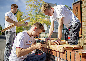 drei Azubis bei der Errichtung mobiler Sitzgelegenheiten aus Holz